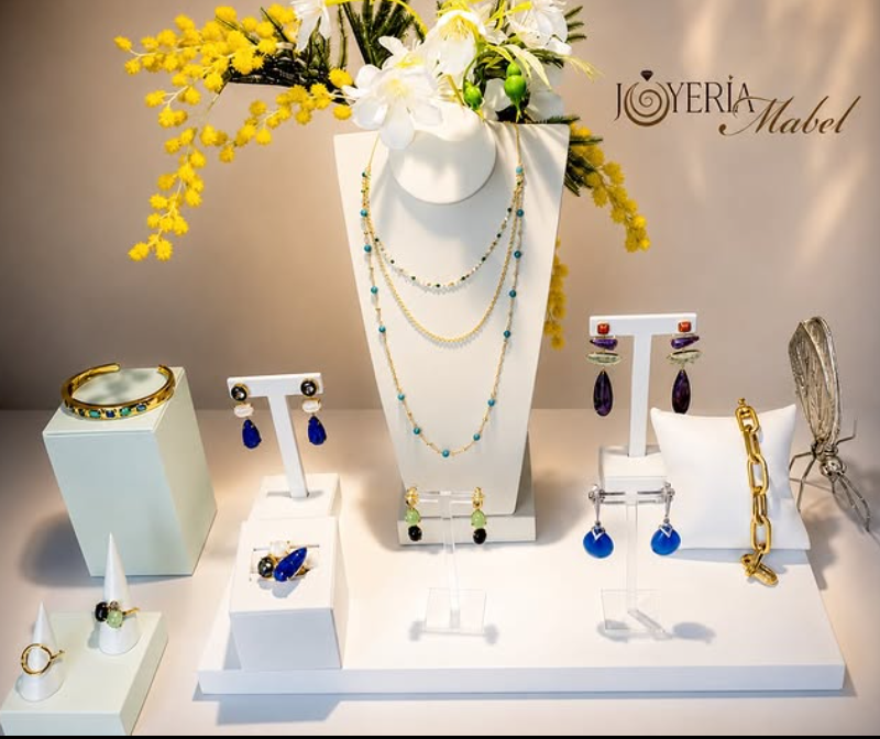 Expositor con collar de capas, pendientes y pulsera en oro, junto a flores