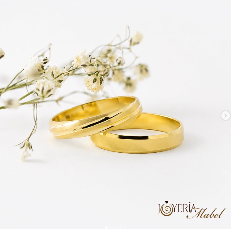 Alianzas de oro sobre superficie blanca junto a flores secas